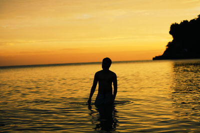 Silhouette of man submerged in water during sunrise