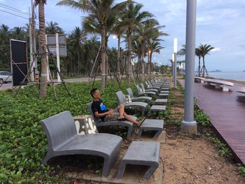 Man sitting on chair by palm trees