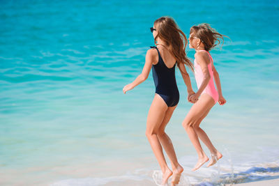 Rear view of sisters jumping in sea