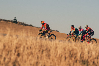 People riding bicycle on field against sky