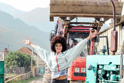 Portrait of smiling young woman with arms raised standing against earth mover
