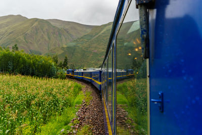 Train by field against green mountains
