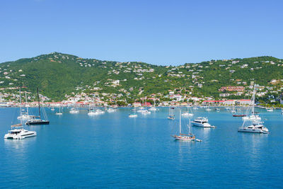 Boats in sea against clear blue sky