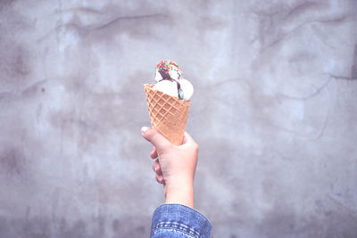 Cropped hand of woman holding ice cream cone against wall