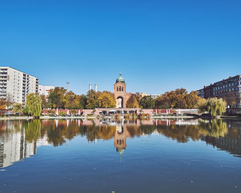 Reflection of building in lake against clear blue sky