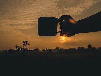 Silhouette person holding sun on field against sky during sunset