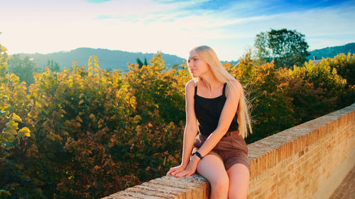 Full length of young woman standing on retaining wall against sky