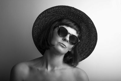 Portrait of young woman wearing sunglasses and hat against wall