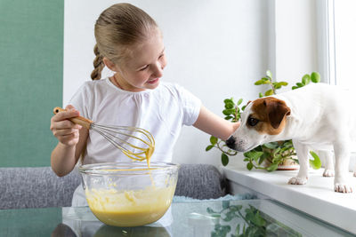 A girl treats dog with whiskey dough from a whisk. hungry dog. for a friend, do not mind. cooking. 