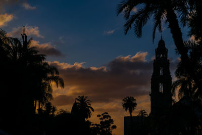 Silhouette of palm trees against cloudy sky