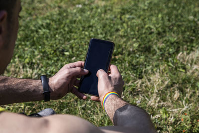 Man with gay flag bracelet holding a smart phone