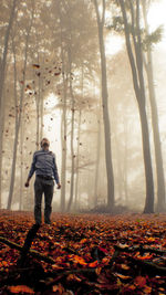 Full length of man standing with leaves in mid-air at forest during autumn