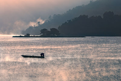 Silhouette man in boat on sea against sky