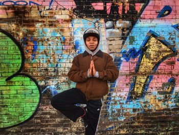 Portrait of young man standing against graffiti wall