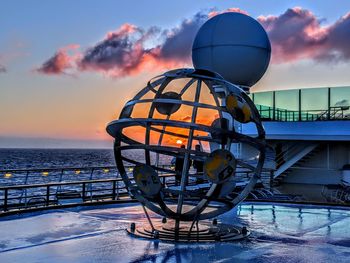 Ferris wheel by sea against sky during sunset