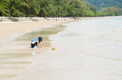 Teenage girl crouching on shore against sea at beach