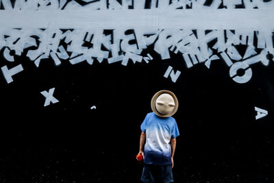 Boy wearing hat while standing against graffiti