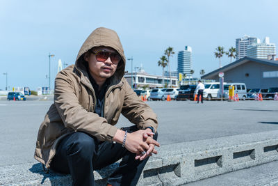 Portrait of mid adult man sitting in city against sky