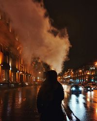 Rear view of woman in illuminated city against sky at night