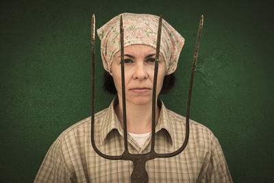 Portrait of woman holding gardening equipment while standing against wall