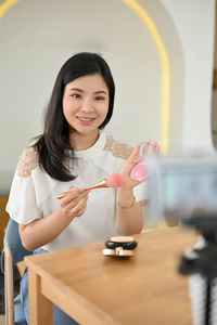 Portrait of young woman using mobile phone while sitting on table