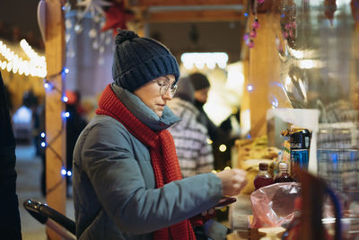 Caucasian woman wearing hat and red scarf buying treats in kiosk at christmas market