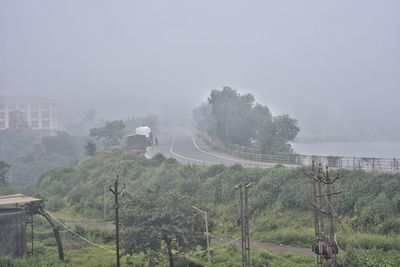 Trees on landscape against sky during foggy weather