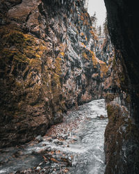 Scenic view of stream flowing by rock formation during winter