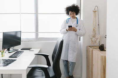 Smiling doctor using smart phone by window in medical office