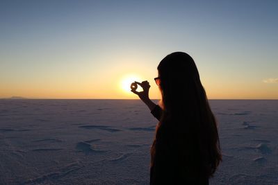 Rear view of woman photographing sea against sunset sky