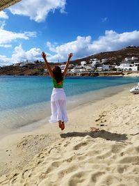 Rear view of woman jumping at beach against sky