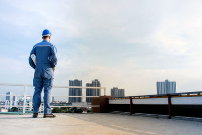 Rear view of male architect standing on footpath in city against sky