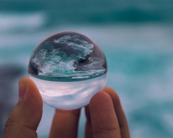 Close-up of hand holding crystal ball against blurred background