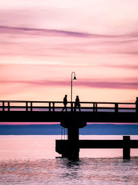 Silhouette people on pier over sea against sky during sunset