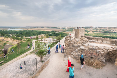 People walking in city against cloudy sky