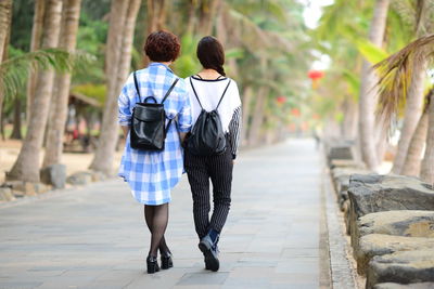 Rear view of women walking on road amidst palm trees