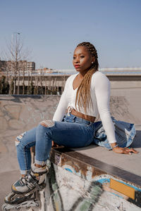 Full length of woman sitting on retaining wall against sky