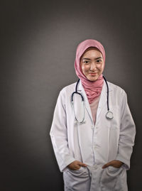 Portrait of doctor standing against gray background