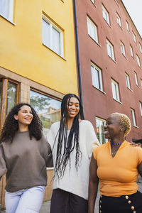 Smiling multiracial young female friends walking by building while hanging out on weekend