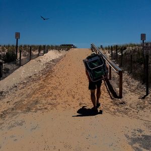 Rear view of man on sand against clear sky