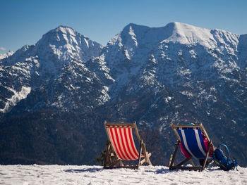 Chairs on snow covered field against mountains and sky