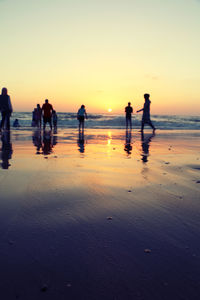 Silhouette people on beach against sky during sunset