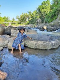 Portrait of cute girl sitting on stone in water