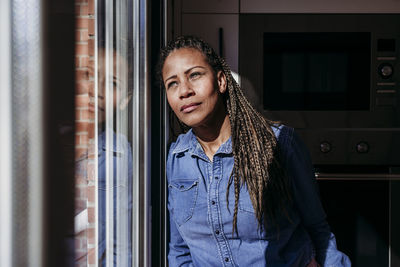 Thoughtful mature woman leaning on glass door at home