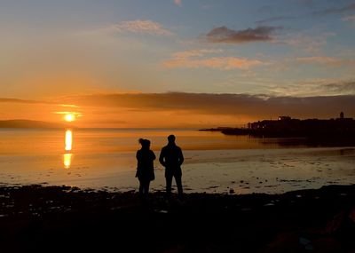 Silhouette friends standing on beach against sky during sunset