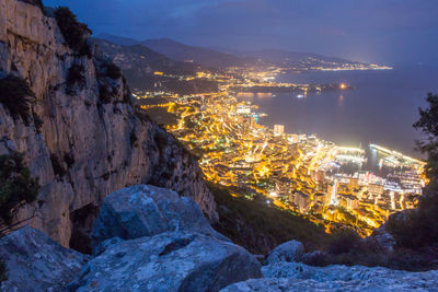 Illuminated city by mountains against sky at night