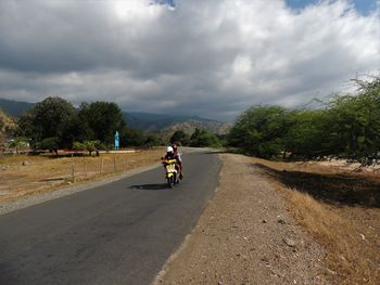 Friends riding motorcycle on road against cloudy sky