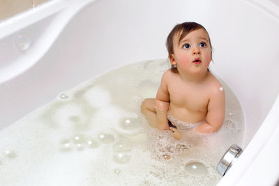 Baby boy sitting in bath with water and foam