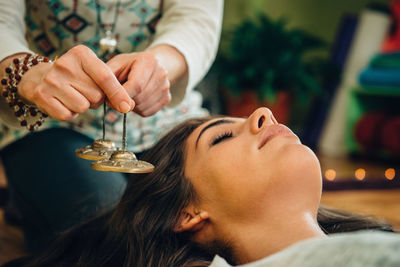 Midsection of therapist holding bells by young woman at spa