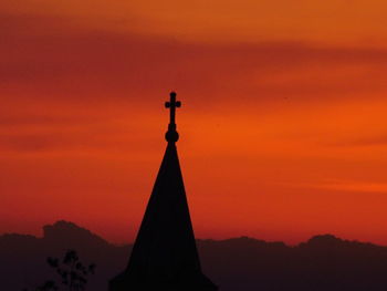 Silhouette cross against orange sky